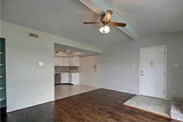 Living room with vaulted beamed ceiling, ceiling fan and front entry; kitchen beyond
